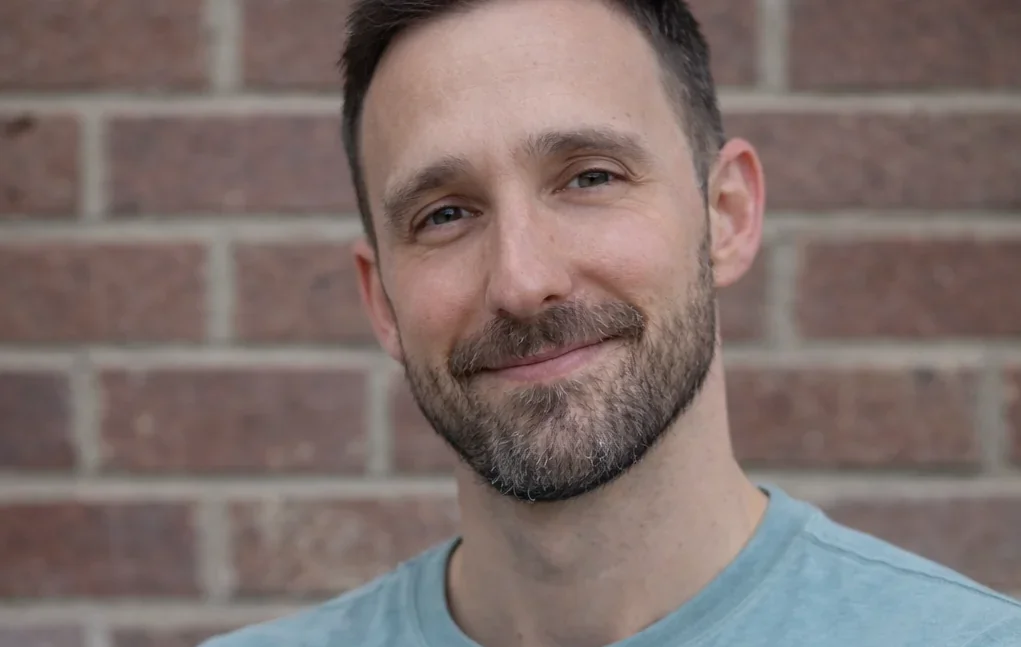 Marc Simon smiling in a head-and-shoulders portrait against a red brick wall.