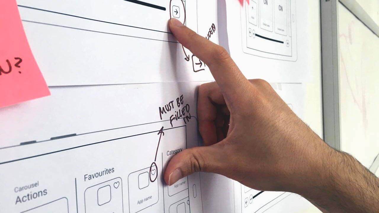 Hand pointing at user experience (UX) wireframes of Breezie's features.